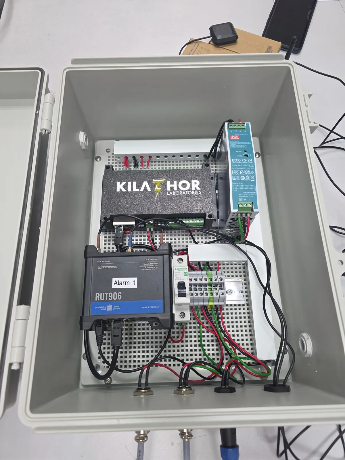 Open alarm unit: KiLATHOR controller, Teltonika RUT906 4G router labelled Alarm 1, a 24 V DIN-rail power supply, breaker and terminal blocks