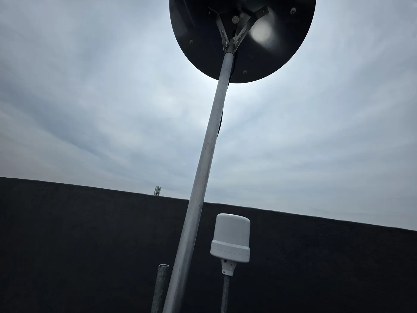 A dish-shaped VHF antenna and a GPS puck against a cloudy sky