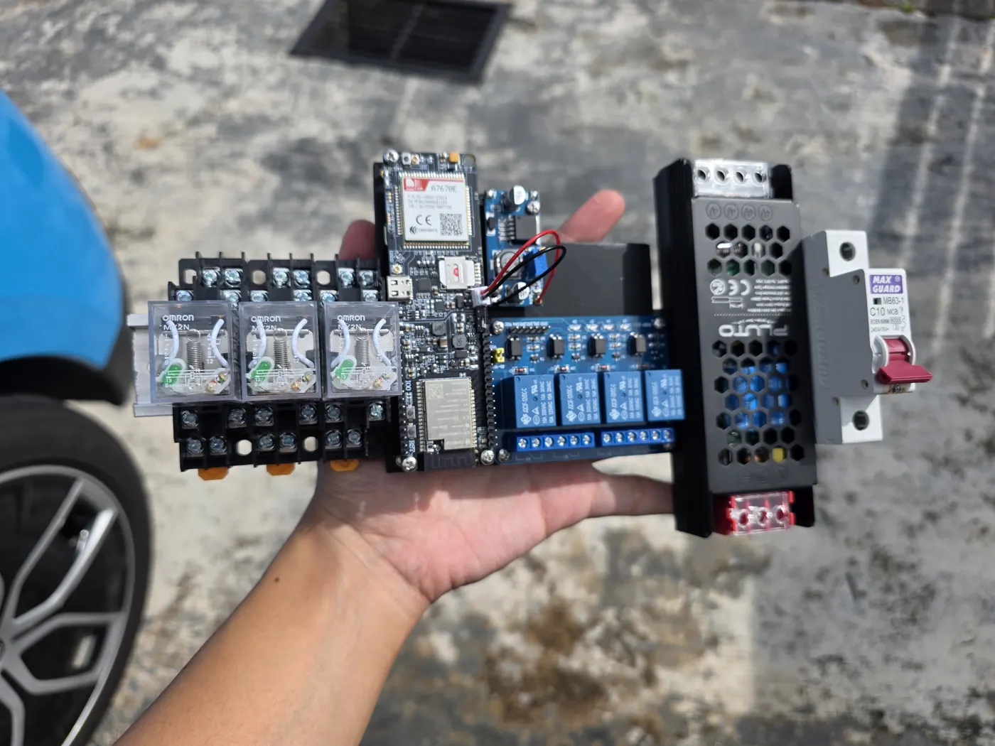 A hand holding an assembled alarm relay kit with breakers and relays